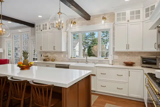 Burrillville, RI kitchen remodel with white shaker cabinets, a stained wood island with white top, dark ceiling beams and glass globe pendants