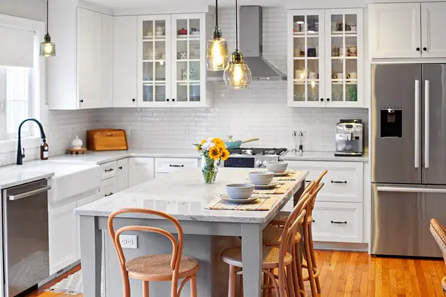 Barrington, RI kitchen with white cabinets, glass-front uppers, a gray island with bentwood stools and amber glass pendants