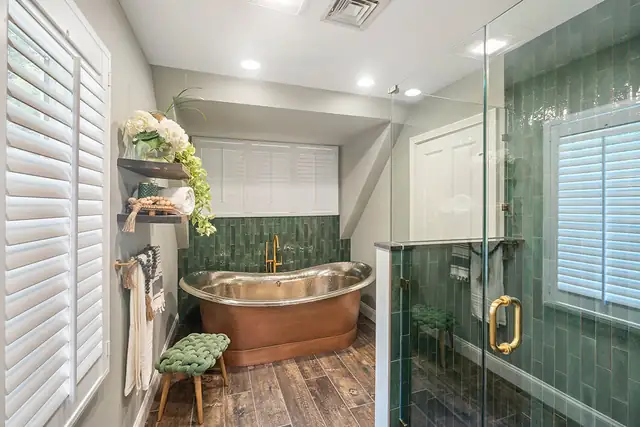East Greenwich, RI bathroom with a copper soaking tub, green tile walls, a frameless glass shower and plantation shutters