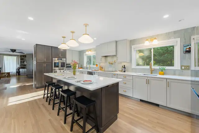 Glocester, RI kitchen with a dark island and black stools, gray cabinets, sage green wall tile and brass schoolhouse pendants