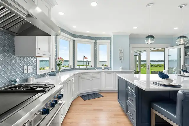Kitchen with blue arabesque backsplash tile, a navy island, a professional range and bay windows facing the water