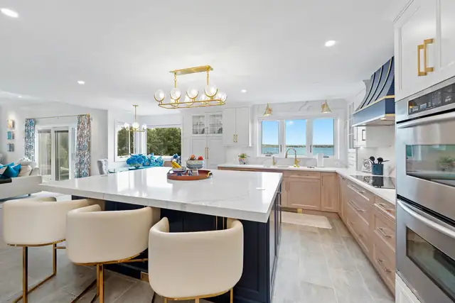 Waterfront kitchen with white oak cabinets, a navy island with white quartz top, cream swivel stools and a brass linear chandelier