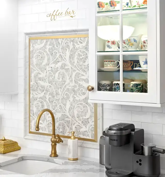 North Kingstown, RI coffee bar with a white glass-front cabinet, gold faucet, scrolled tile panel and white subway backsplash