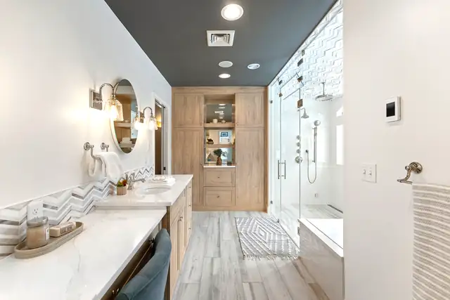 East Greenwich, RI primary bathroom with a frameless glass walk-in shower, a wood built-in cabinet, round mirror and dark gray ceiling