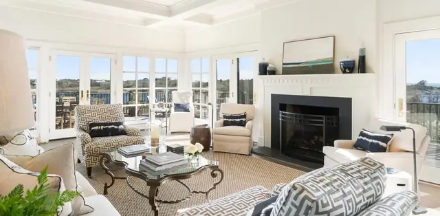 Rhode Island living room remodel with a white fireplace surround, coffered ceiling and a wall of windows facing the water