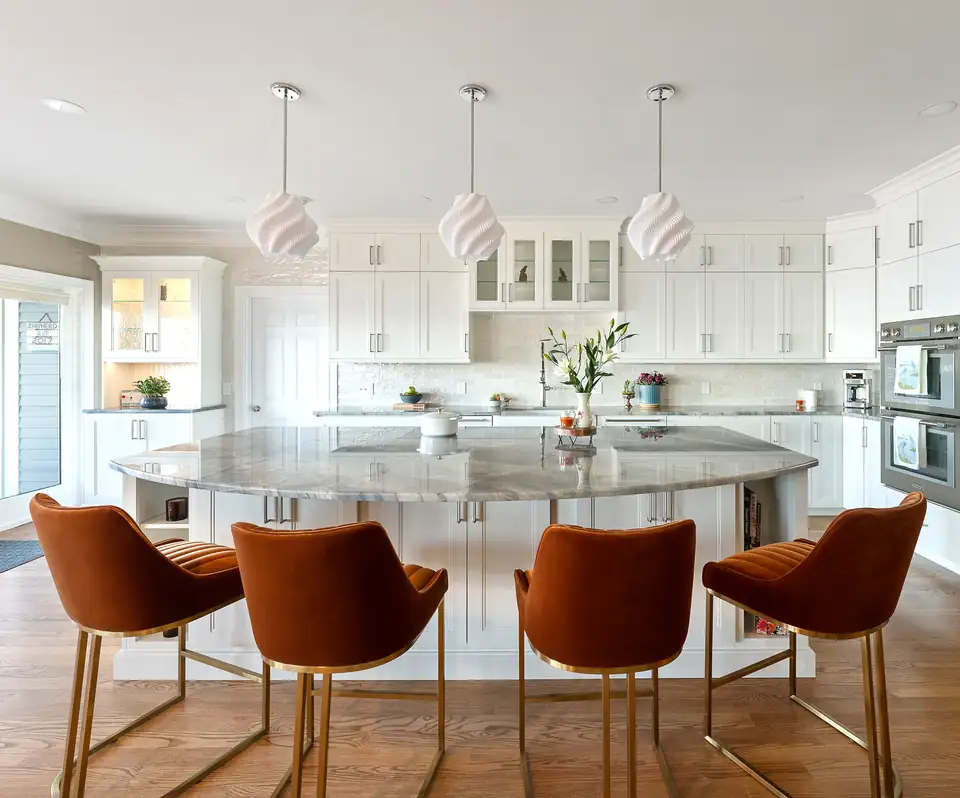 Kitchen and bath remodeling Warwick team's work in Portsmouth, RI: a kitchen with a round stone-topped island, rust velvet stools, white pendants and white cabinets