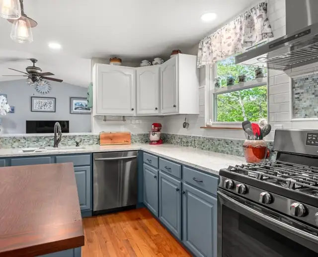 Warwick, RI kitchen with blue-gray lower cabinets, white uppers, a glass mosaic backsplash and a wood-topped island